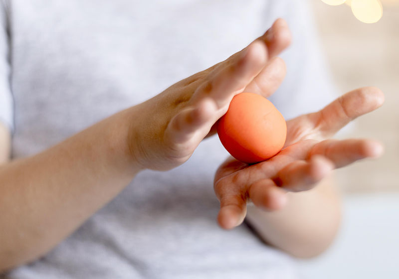 Mãos de criança fazendo uma bola com massinha de modelar laranja